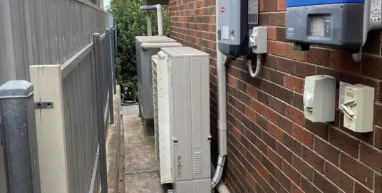 Gray rectangular solar inverter mounted on a brick wall.